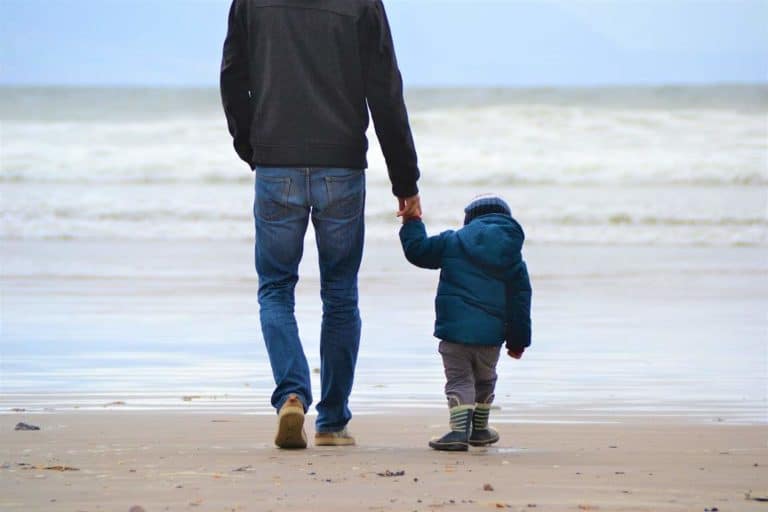 dad walking along the beach holding his sons hand