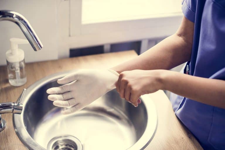 woman putting on gloves at a sink