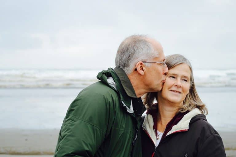 elderly man kissing partner on the cheek at the beach