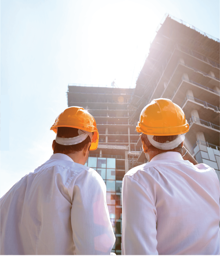Two business men wearing a construction helmet looking up at a building under construction