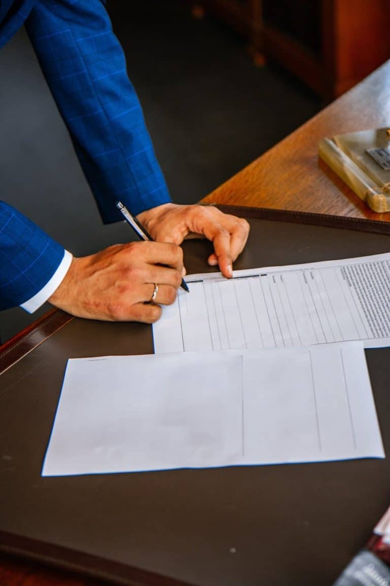 business man standing at desk, leaning over and signing a documents