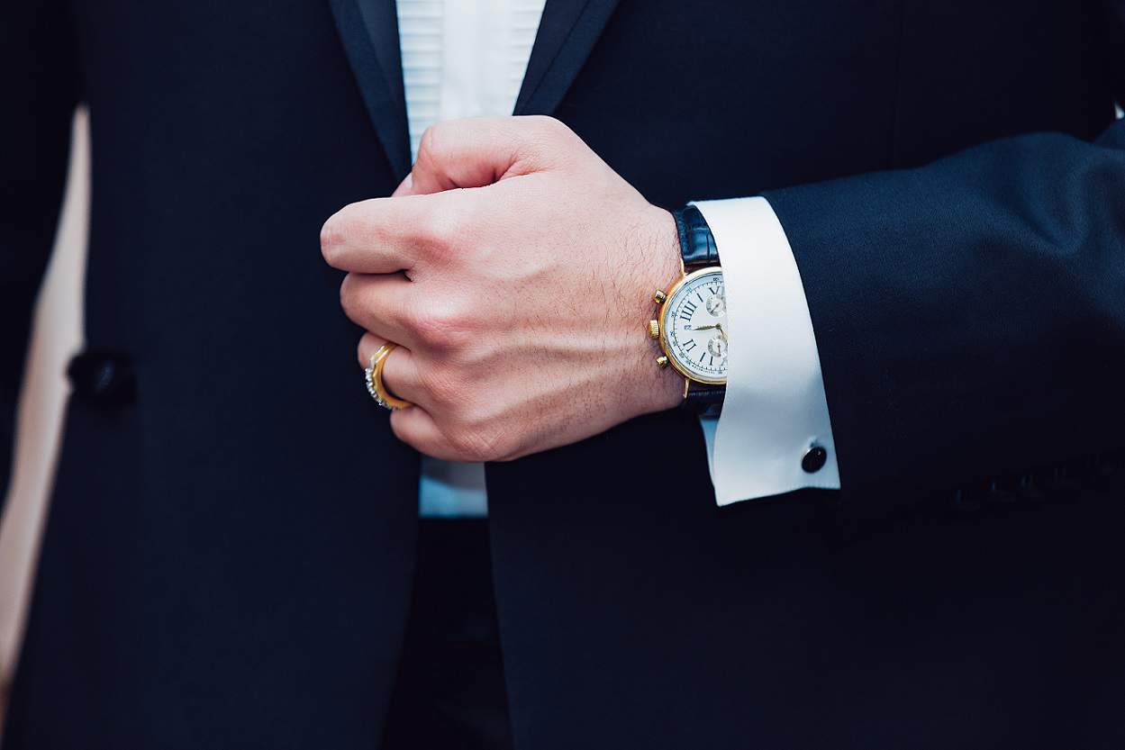close up of man in a suit with an gold watch and gold ring