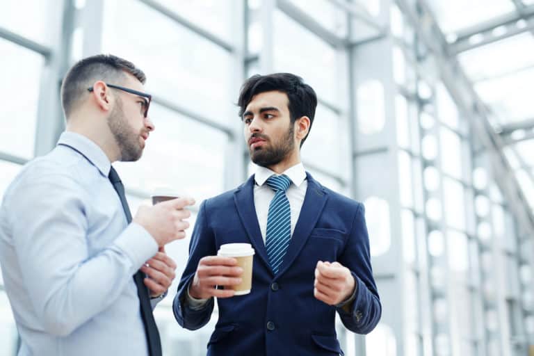two business men talking in an office building while holding a coffee