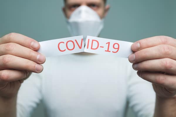 Worried man wearing a respiratory mask, holding a ripped Coronavirus Covid-19 sign