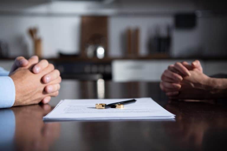 Partial view of couple sitting at table with clenched hands near divorce documents
