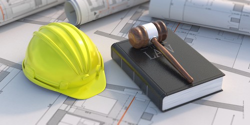 construction hat next to a book of law and judges gavel on top of construction plans
