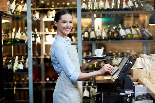 Young cheerful waitress registrating an order and carrying it to the client