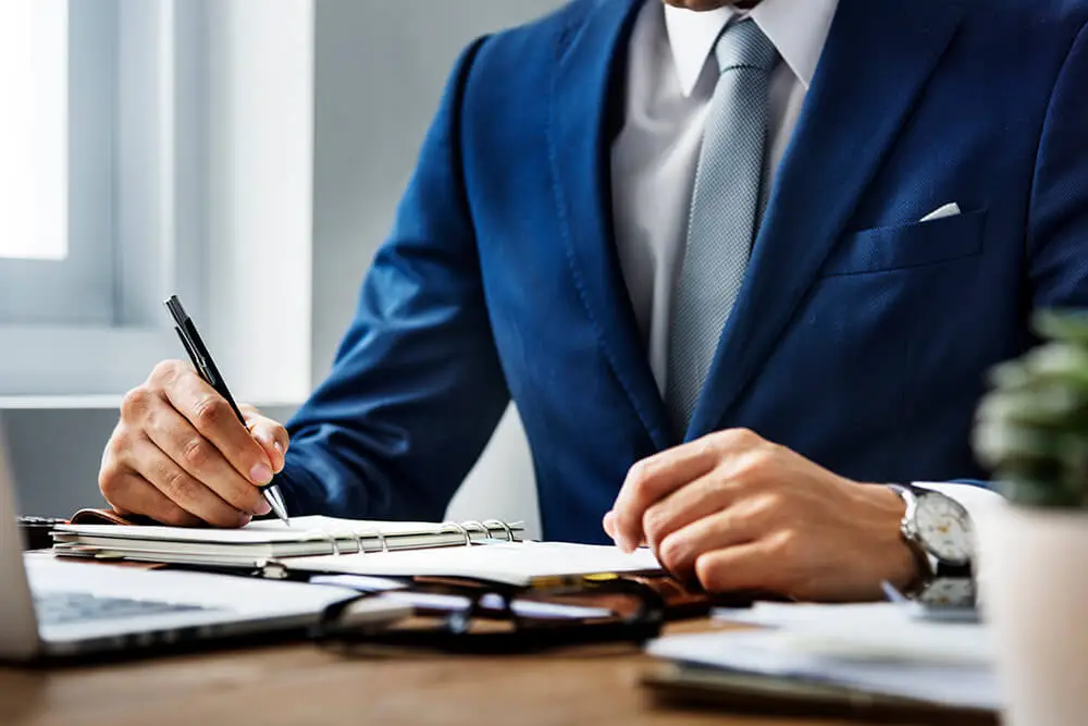 man in blue business suit writing in notebook