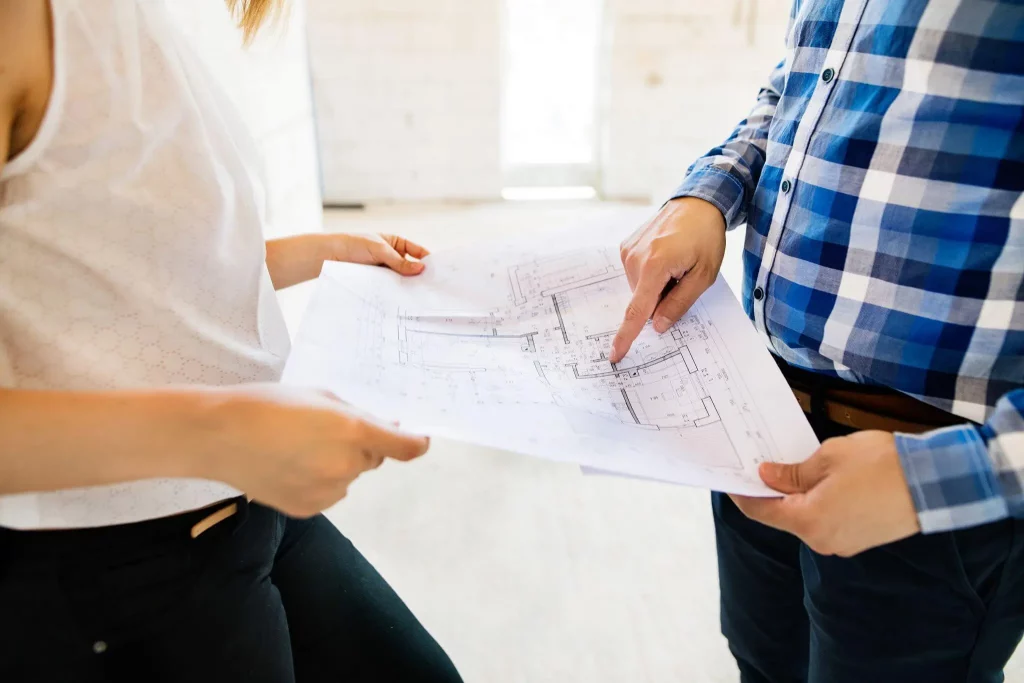 man and woman holding and pointing at building plans