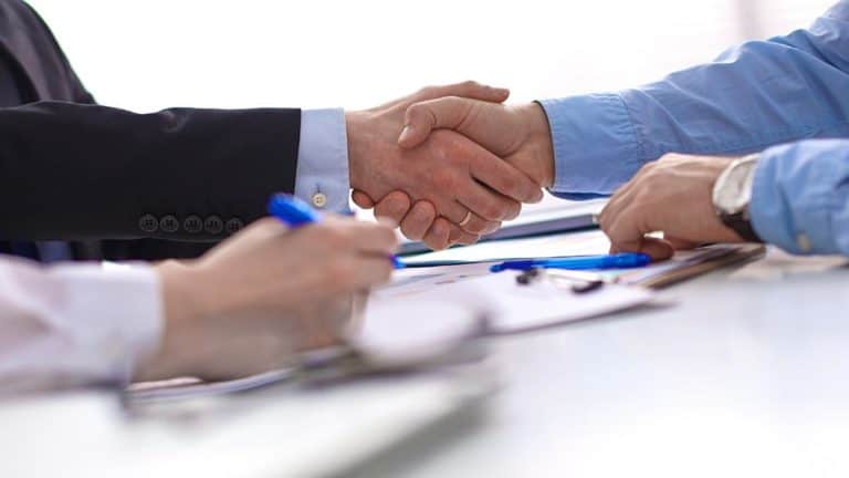 Two business people shaking hands over a table to celebrate the release of New REIQ Residential Contracts on 20 January 2022.