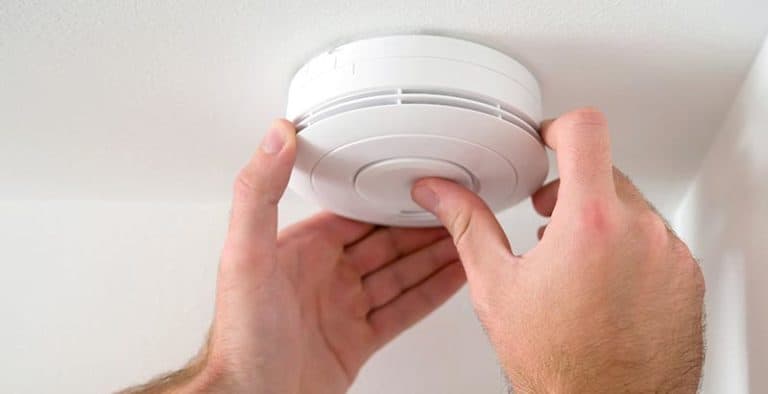 A man installing a smoke detector to comply with the New Smoke Alarm Requirements from 1 January 2022.
