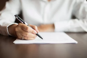 A woman drafting a Share Sale Agreement or Business Sale Agreement with a pen.