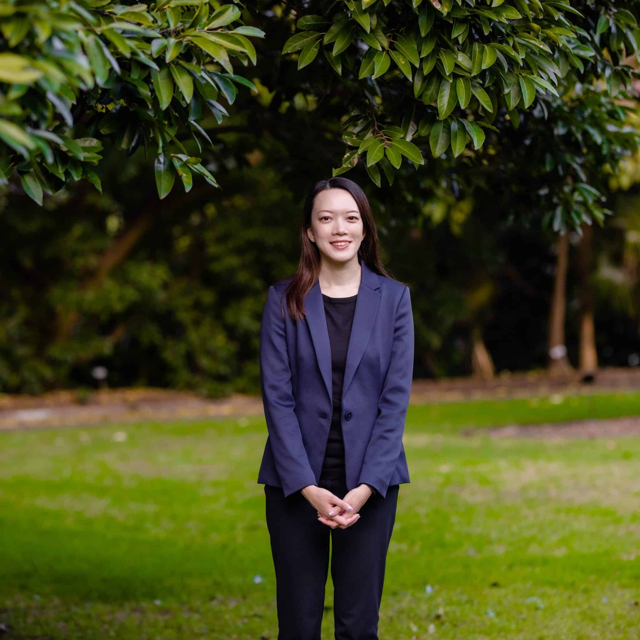Jade Tsang, a young woman in a business suit, standing in front of a tree.