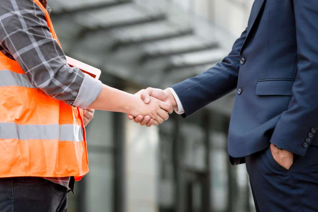 Two construction workers shaking hands in front of a building undergoing bankruptcy proceedings.